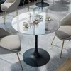 A round marble-top table with a black pedestal base, surrounded by chairs in a room with marble-patterned flooring. Produktbild-Vorschau