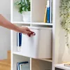 A hand is shown reaching for a white storage bin on a shelf. Produktbild-Vorschau
