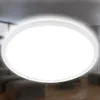 A bright, circular LED ceiling light is shown against a blurred background of a living room. Produktbild-Vorschau