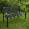 A black metal garden bench sits on a green lawn with lush green bushes and red roses in the background. Anteprima dell’immagine prodotto