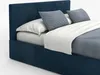 A close-up view of a dark blue upholstered bed with white bedding and light blue pillows. Produktbild-Vorschau