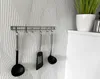 Kitchen utensils hanging on a wall rack against a patterned wallpaper. Produktbild-Vorschau