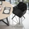 A black velvet armchair is placed next to a round wooden dining table, set for a meal with a cake and place settings. The scene is set in a modern interior with large windows overlooking a cityscape. Náhled obrázku produktu