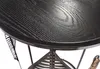 A close-up view of a black wooden tabletop with visible wood grain, resting on a metal frame with decorative leaf motifs. Produktbild-Vorschau