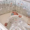 A baby sleeping in a crib with a patterned blanket and bumper pads. Produktbild-Vorschau