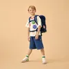 A young boy wearing a backpack and a t-shirt with cartoon cat faces, standing against a plain background. Produktbild-Vorschau