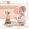 A baby is playing with a stacking toy on a bed. Voir les images du produit