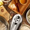 A close-up overhead view of baking ingredients and a hand mixer arranged on a wooden surface. Produktbild-Vorschau