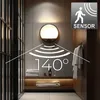 A modern bathroom with a wall-mounted LED lamp featuring a motion sensor. Voir les images du produit
