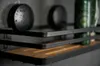 A close-up shot of a bathroom shelf with two round black containers and a green bottle. Produktbild-Vorschau