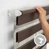 A hand is shown installing a brown and white striped roller blind onto a wall bracket. Produktbild-Vorschau