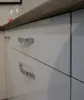 A close-up view of a modern kitchen cabinet with glossy white drawers and silver handles. Produktbild-Vorschau