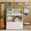 A children's room with a white bookshelf filled with books and toys, a wooden ruler on the left, and a light blue backpack hanging on the wall. Náhľad obrázku produktu