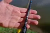 A hand holding a fishing rod near the water. Produktbild-Vorschau