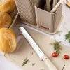 A kitchen set with knives and a cutting board, along with bread rolls and herbs. Produktbild-Vorschau