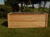 A wooden planter box sits on a grassy lawn with trees in the background. Produktbild-Vorschau