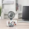 A portable fan with a smartphone attached to its base, showing a group of people dancing on the screen. A laptop is visible in the background. Náhled obrázku produktu