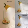 A desk lamp shaped like a flower, shown in different lighting conditions on a nightstand. Produktbild-Vorschau