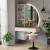 A modern vanity table with a round LED mirror, shelves, and a pink stool in a well-lit room. Voir les images du produit