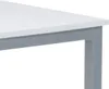 A close-up view of the corner of a table, showing the white tabletop and gray legs. Náhled obrázku produktu