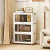 A white storage cabinet with three clear doors, filled with books and decorative items, placed in a living room setting next to a sofa and a floor lamp. Náhľad obrázku produktu