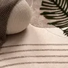 A close-up view of a textured rug with a woven pouf and a shadow of a leaf. Produktbild-Vorschau