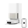A white robot vacuum cleaner with a silver accent is docked in its charging station. A smartphone displaying a black logo on a white screen is placed to the right of the charging station. Produktbild-Vorschau