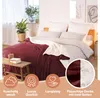 A bed with a dark red and cream blanket, pillows, and a small wooden table with books and a plant. Podgląd zdjęcia produktu