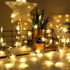 A decorative string of star-shaped lights is displayed on a surface, with a star-shaped lamp and a potted plant in the background. Náhled obrázku produktu