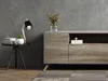 A modern living room scene featuring a media console, a side table with a lamp and plant, and a textured gray wall. Produktbild-Vorschau