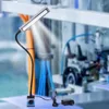 A magnetic LED work light with a flexible gooseneck is shown in a factory or industrial setting. Podgląd zdjęcia produktu