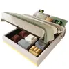 A bed with its storage compartment open, revealing folded linens and towels. Produktbild-Vorschau