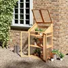 A wooden mini greenhouse filled with plants, placed outdoors next to a brick wall and a window. Voir les images du produit