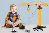 A young boy is sitting on the floor next to a large yellow toy crane. Náhľad obrázku produktu