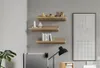 Three wooden shelves mounted on a gray wall, decorated with books, toys, and a framed picture. A desk lamp and a plant are visible in the foreground. Produktbild-Vorschau