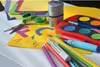 A collection of art and craft supplies, including colored paper, scissors, pencils, and a watercolor paint set, arranged on a white surface. Produktbild-Vorschau