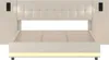 A front view of a beige upholstered bed frame with a tufted headboard and integrated side units containing black electrical outlets. The bed frame has a slatted mattress support and a yellow LED light strip along the bottom. Anteprima dell’immagine prodotto