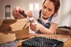 A woman is using a ratchet screwdriver to work on a wooden box. Produktbild-Vorschau