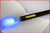 A black LED inspection lamp with a COB stripe and UV spot is shining a blue light onto a grid-lined notebook. Podgląd zdjęcia produktu