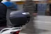 A person riding a scooter with a black top case attached to the back. Anteprima dell’immagine prodotto
