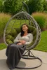 A woman is relaxing in a hanging egg chair outdoors, covered with a blanket. Voir les images du produit