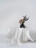 A white silk pillowcase is draped over a pillow, with a small black vase containing a single pink rose and some greenery placed on top. Podgląd zdjęcia produktu