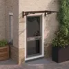 A door canopy mounted above a modern glass door, with brick walls and plants. Anteprima dell’immagine prodotto