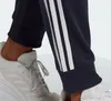A close-up shot of a person's legs wearing navy blue Adidas sweatpants with white stripes and white sneakers. Produktbild-Vorschau