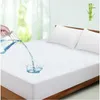 Water being poured onto a white mattress protector on a bed with two pillows. Produktbild-Vorschau