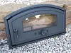 A black cast iron oven door with a glass window is placed on a bed of gravel and rocks. Náhľad obrázku produktu