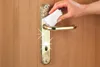 A hand is cleaning a door handle with a white wipe. Produktbild-Vorschau