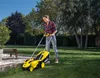 A woman is mowing her lawn with a yellow and black Kärcher battery-powered lawnmower on a sunny day. Produktbild-Vorschau