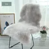 A fluffy gray sheepskin rug draped over a chair, with a framed picture and a small potted plant in the background. Náhled obrázku produktu