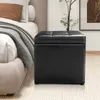 A black storage ottoman is placed next to a bed in a bedroom setting. Podgląd zdjęcia produktu